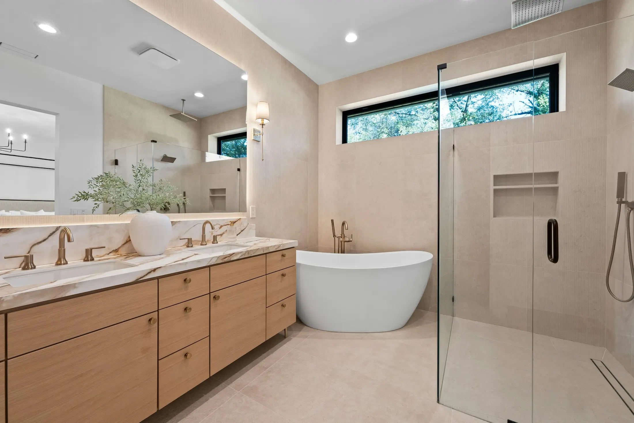 Warm neutral spa bathroom with an oak double vanity, freestanding bath and brass fittings